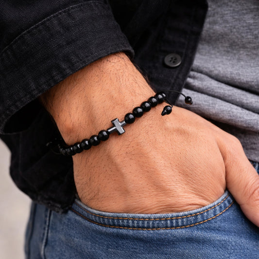 Person wearing a black beaded bracelet with a cross charm on a wrist.