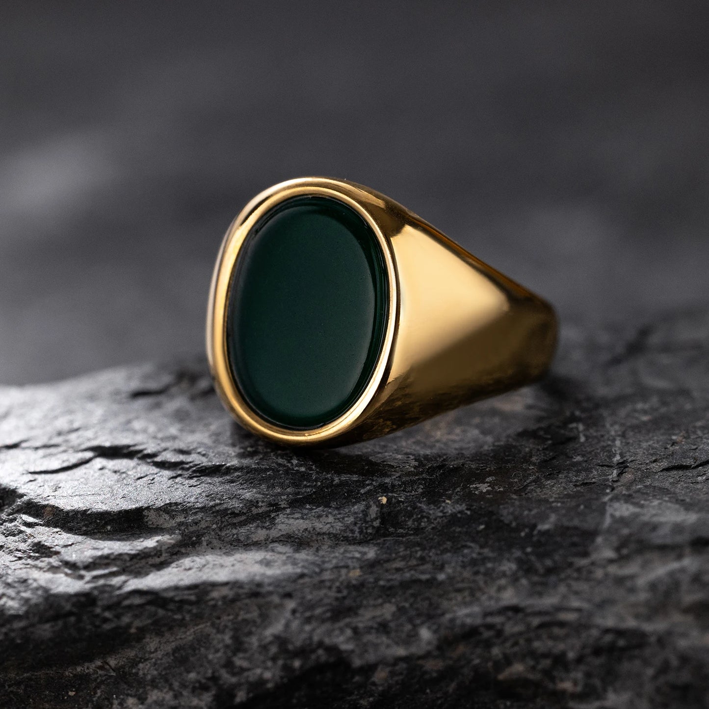 Gold ring with a dark green stone on a textured black surface