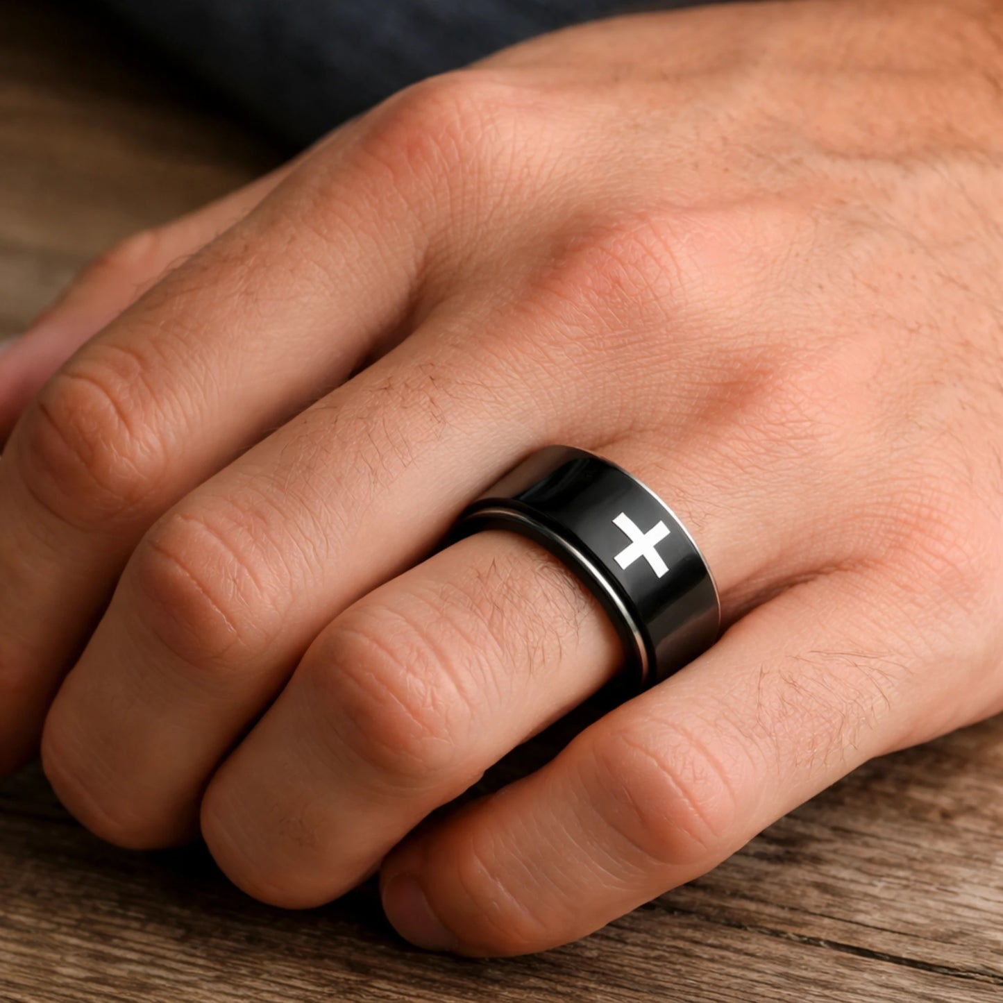 Hand wearing a black ring with a white cross on a wooden surface