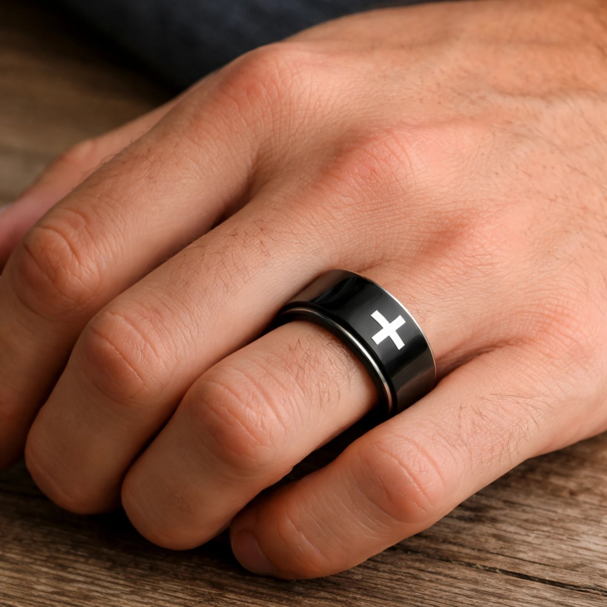 Hand wearing a black ring with a white cross on a wooden surface