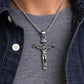 Silver crucifix pendant necklace on a person wearing a denim jacket.