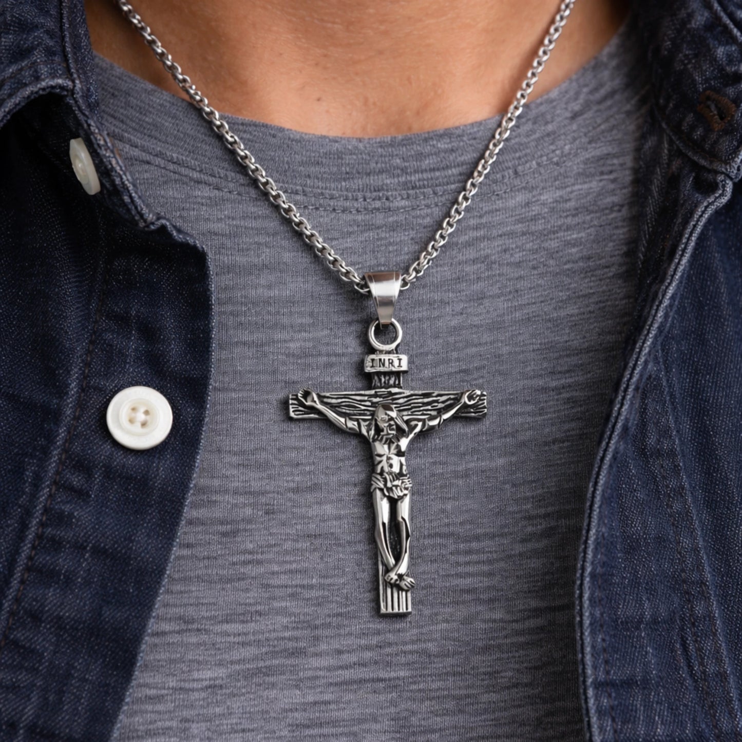 Silver crucifix pendant necklace on a person wearing a denim jacket.
