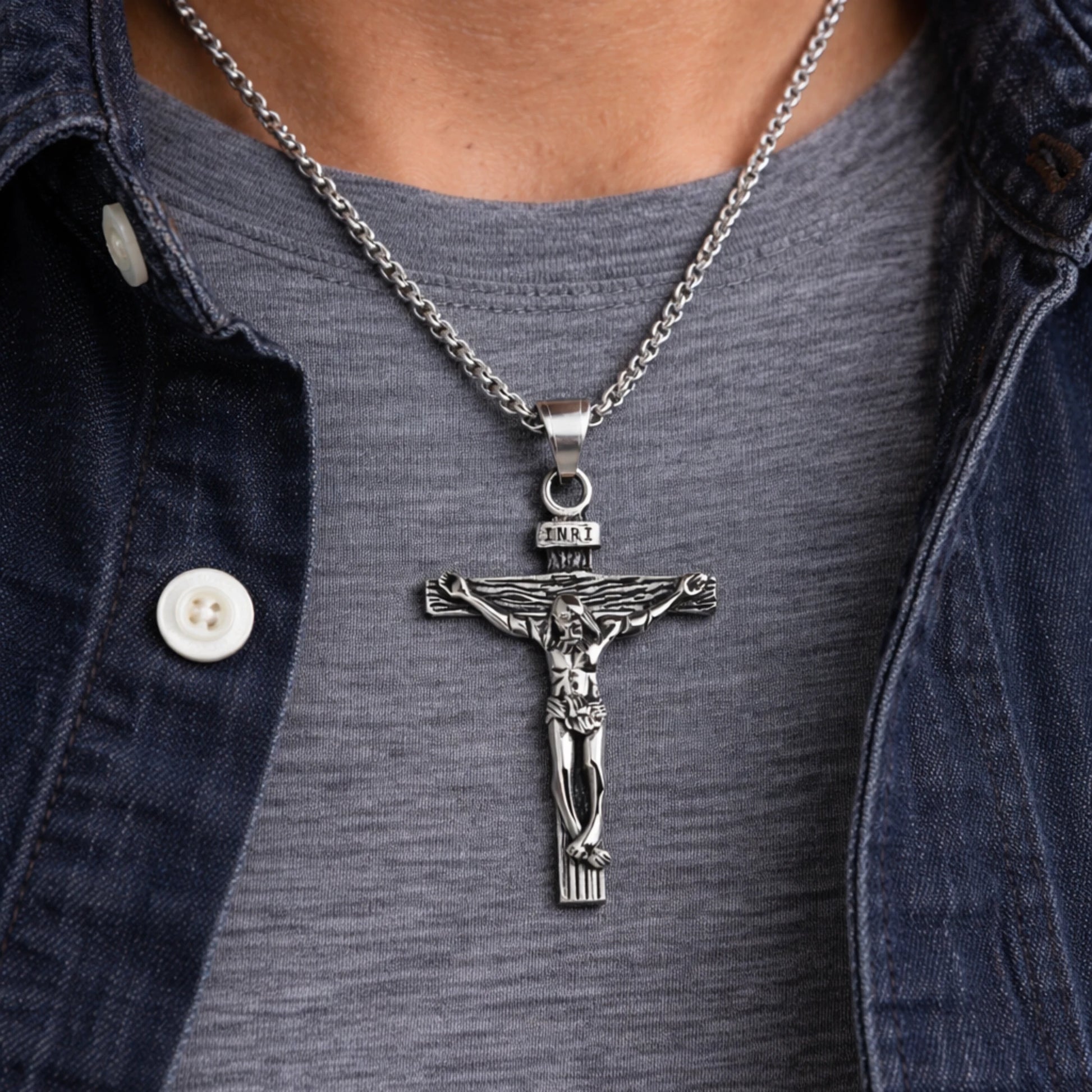 Silver crucifix pendant necklace on a person wearing a denim jacket.