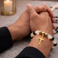 Close-up of hands clasped together with a gold cross bracelet on a textured surface.