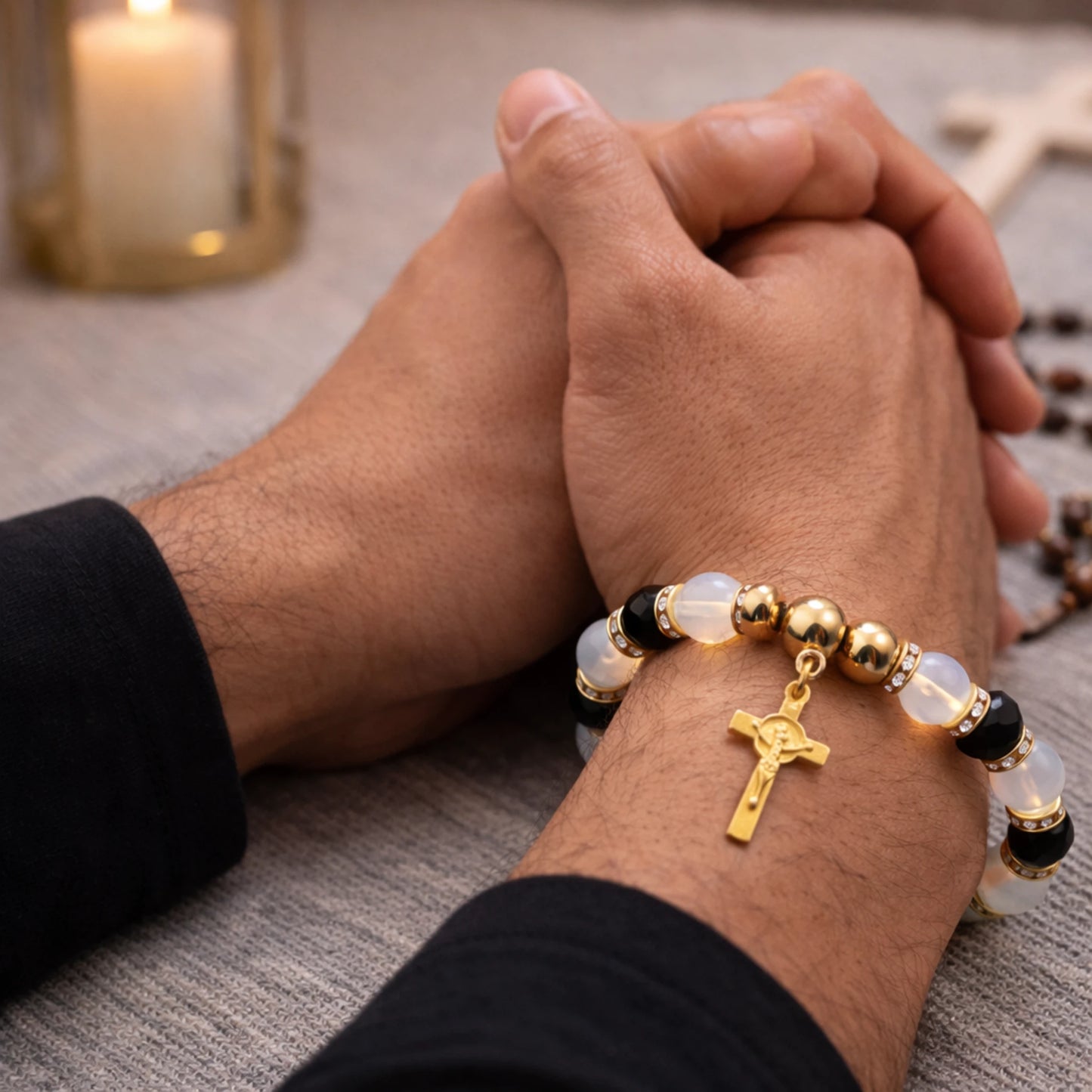 Close-up of hands clasped together with a gold cross bracelet on a textured surface.