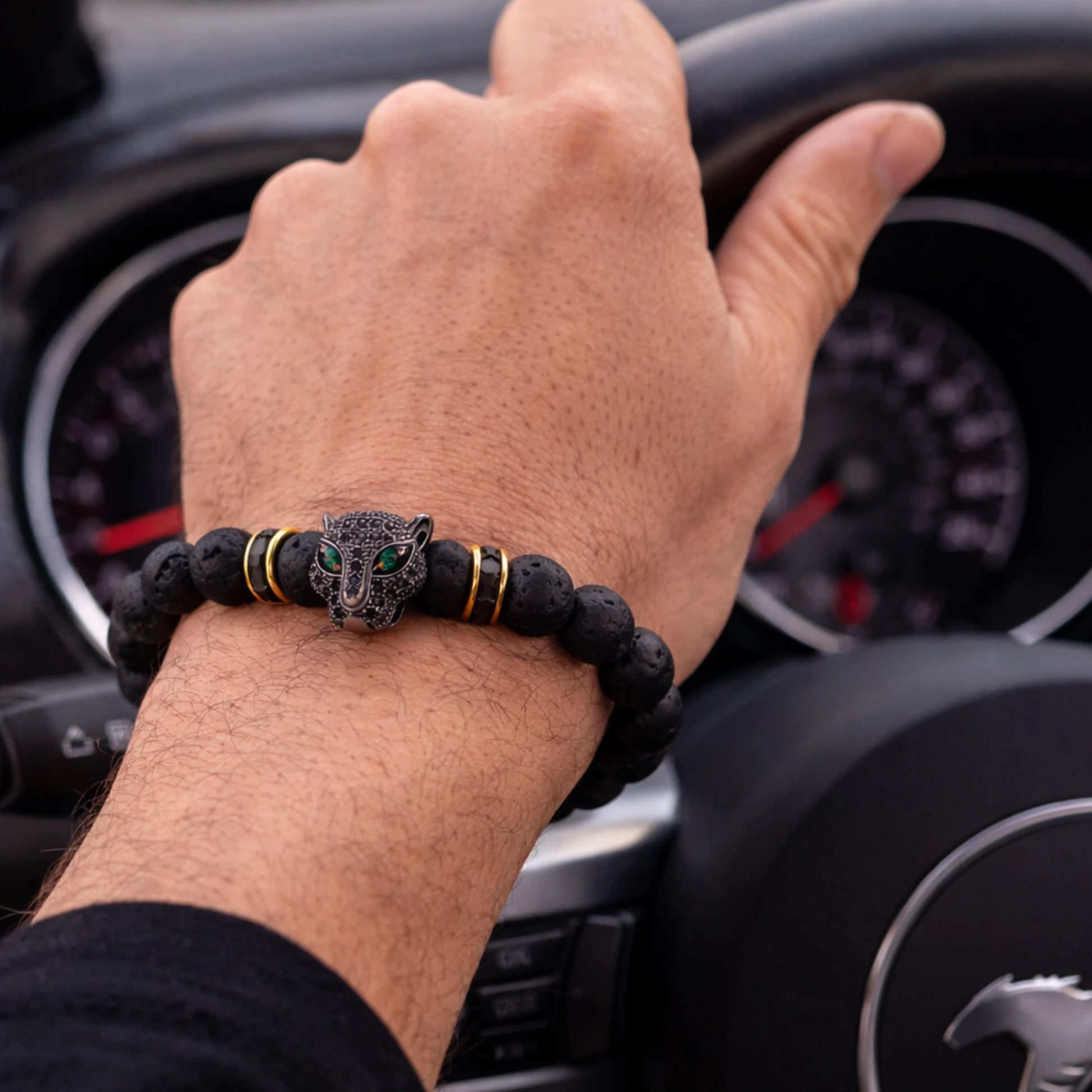 Hand wearing a black beaded bracelet with a panther design in front of a car dashboard.