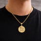Gold necklace with a coin pendant worn by a person on a black shirt.