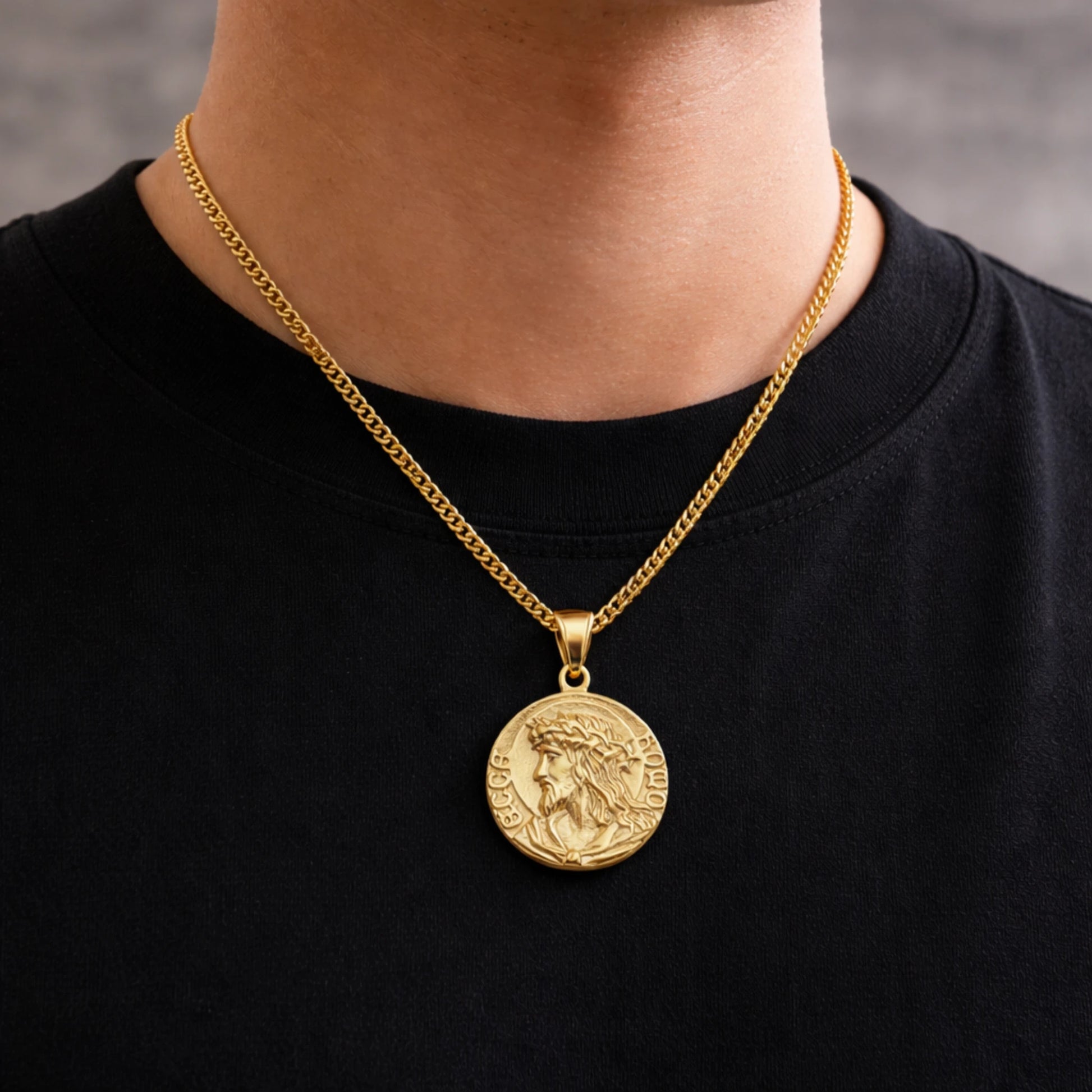 Gold necklace with a coin pendant worn by a person on a black shirt.