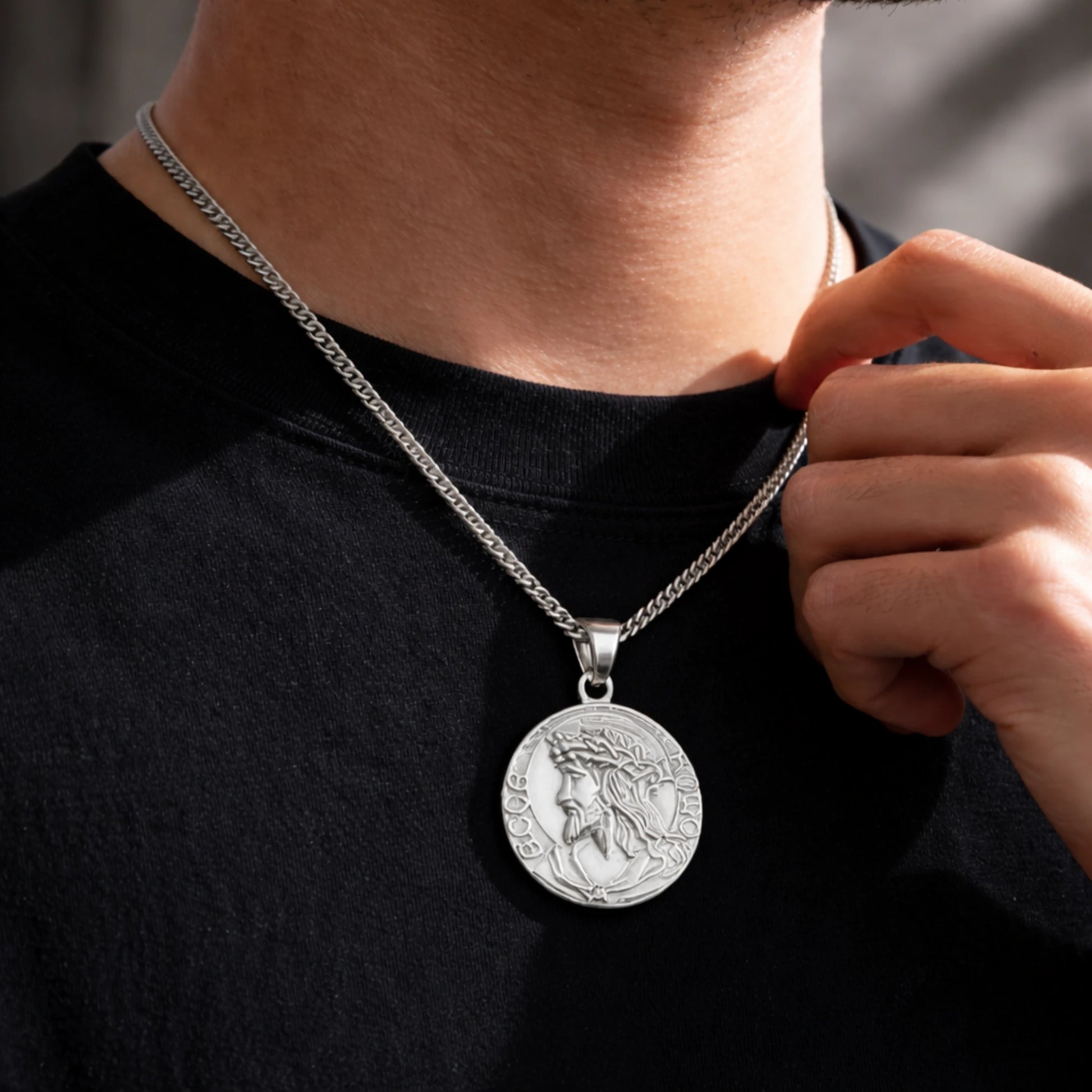 Person wearing a silver necklace with a detailed pendant on a dark background