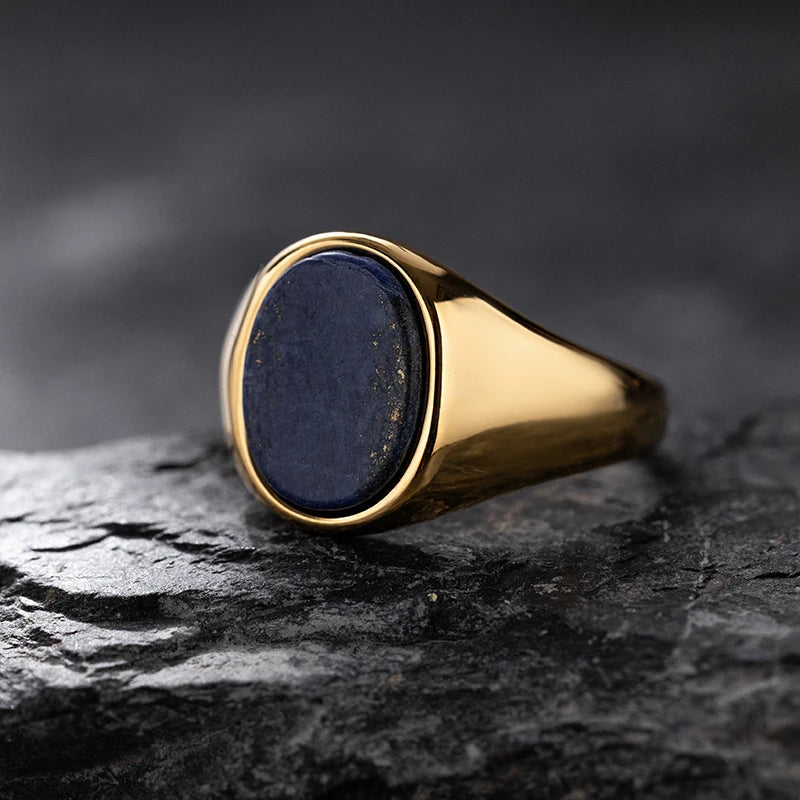 Gold ring with a dark blue stone on a black stone surface