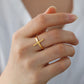 Gold cross ring on a person's finger with a neutral background