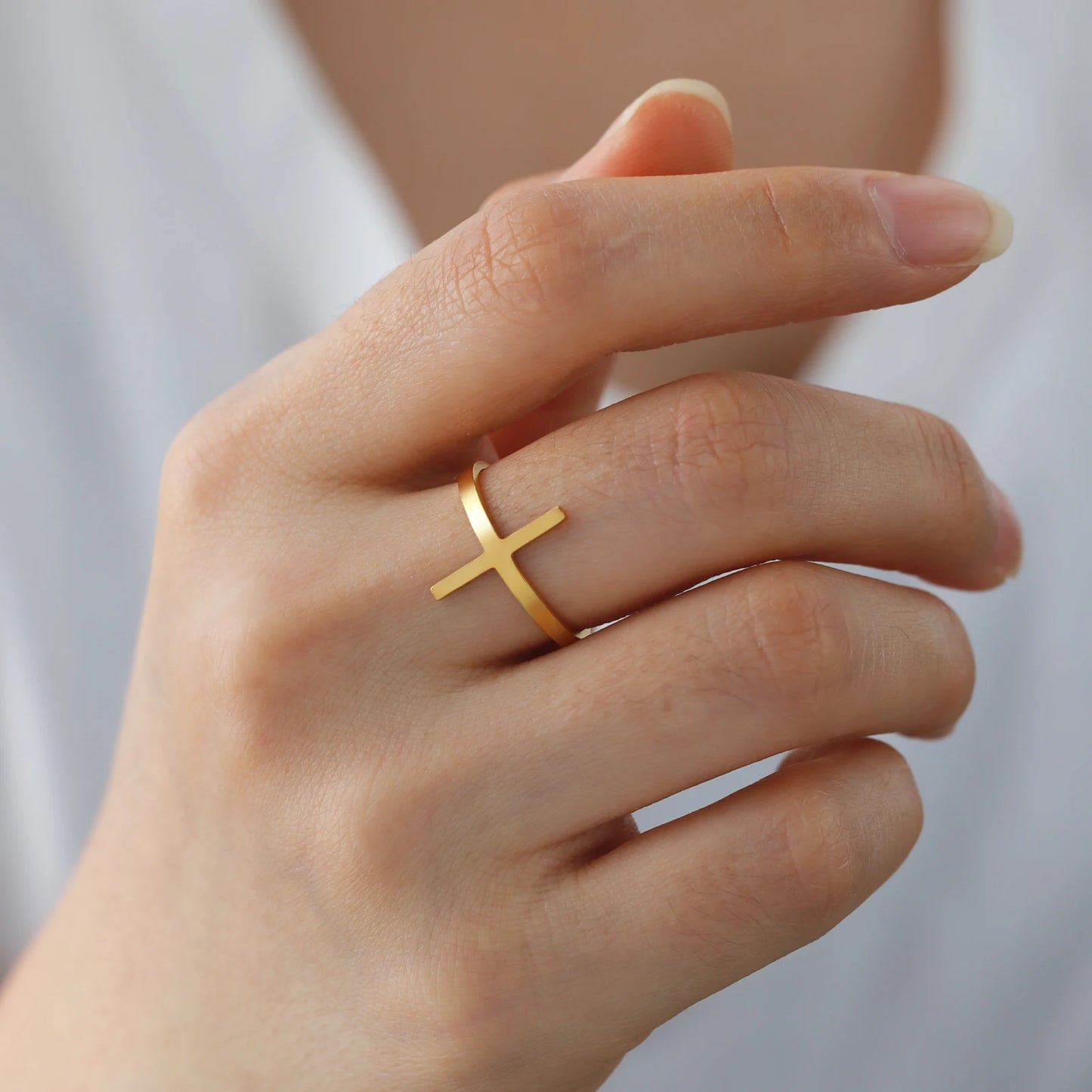 Gold cross ring on a person's finger with a neutral background