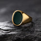 Gold ring with a dark green stone on a textured black surface