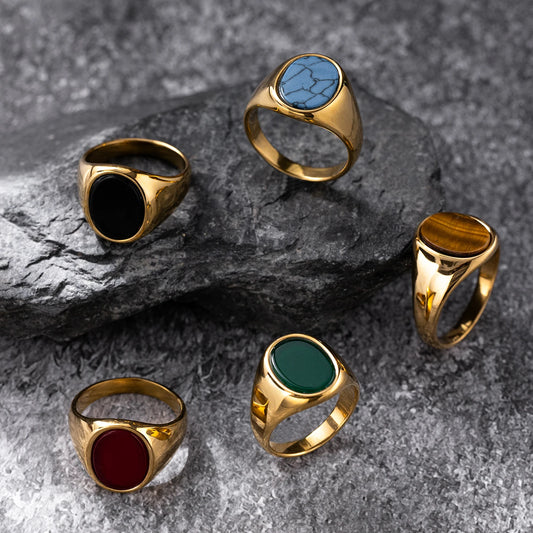 Five gold rings with colored stones on a textured gray surface