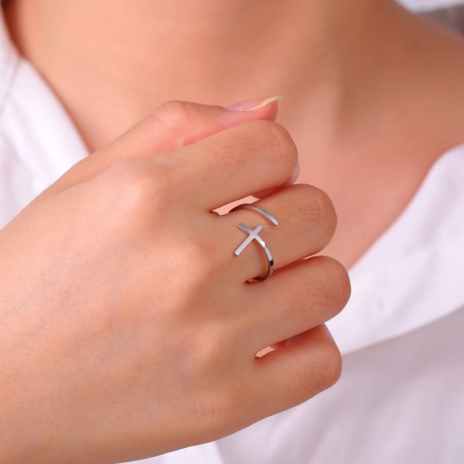 Silver cross-shaped ring on a person's finger with a blurred background