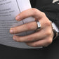 Hand wearing a silver ring with a cross design, holding a book.