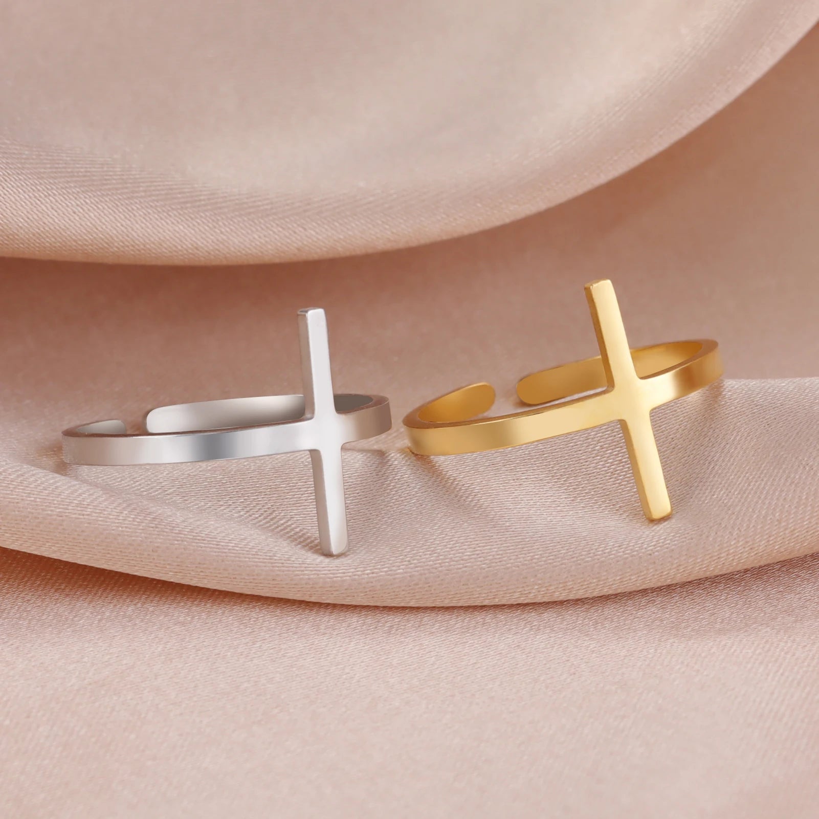 Gold and silver cross-shaped bracelets on a soft pink fabric background