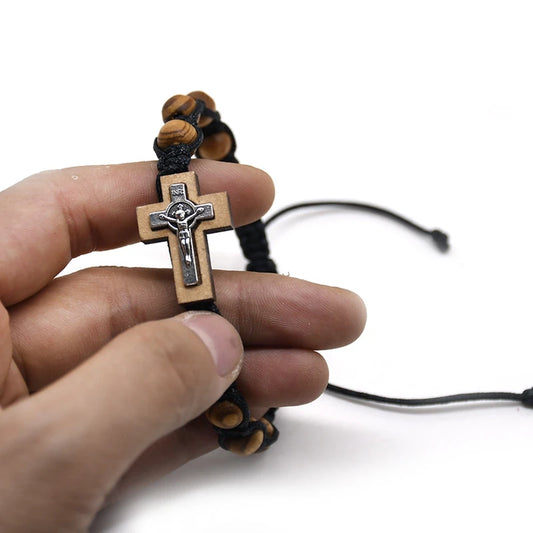 Hand holding a wooden cross pendant with a black cord on a white background