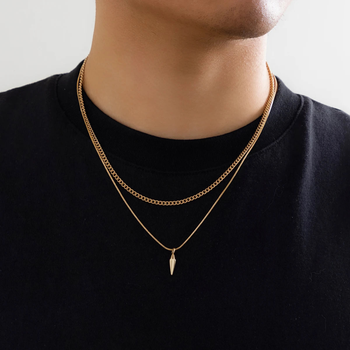 Person wearing a gold chain necklace with a black shirt on a neutral background