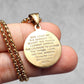 Gold pendant with engraved text held in a hand against a neutral background