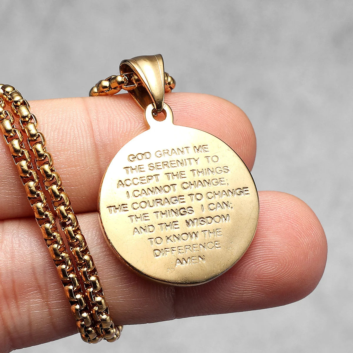 Gold pendant with engraved text held in a hand against a neutral background